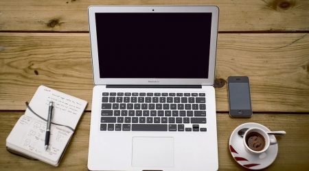 Laptop computer, notepad and cup of coffee on a desk
